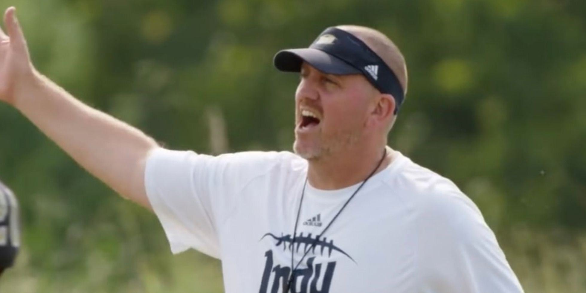 Coach Jason Brown wears visors and a white T-shirt on the field at Last Chance U