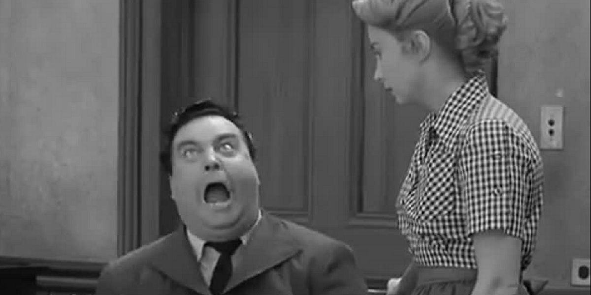 Ralph Cramden (Jackie Gleason) angrily shouts at the kitchen table, while his wife Alice (Audrey Meadows) patiently watches.