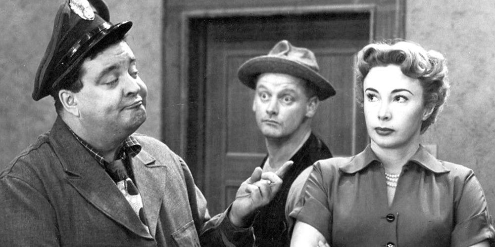 Jackie Gleason as Ralph Cramden, pointing at Alice (Audrey Meadows), while Ed Norton (At Carney) pokes his head between the two