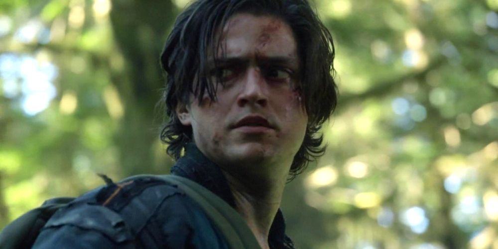 Finn Collins stands in the woods on The 100